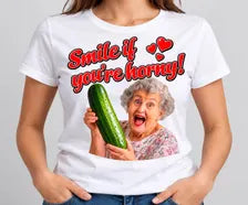 T-shirt branca Smile If You're Horny com frase vermelha e senhora a segurar um pepino.