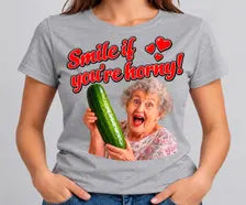 T-shirt cinzenta Smile If You're Horny com frase vermelha e senhora a segurar um pepino.